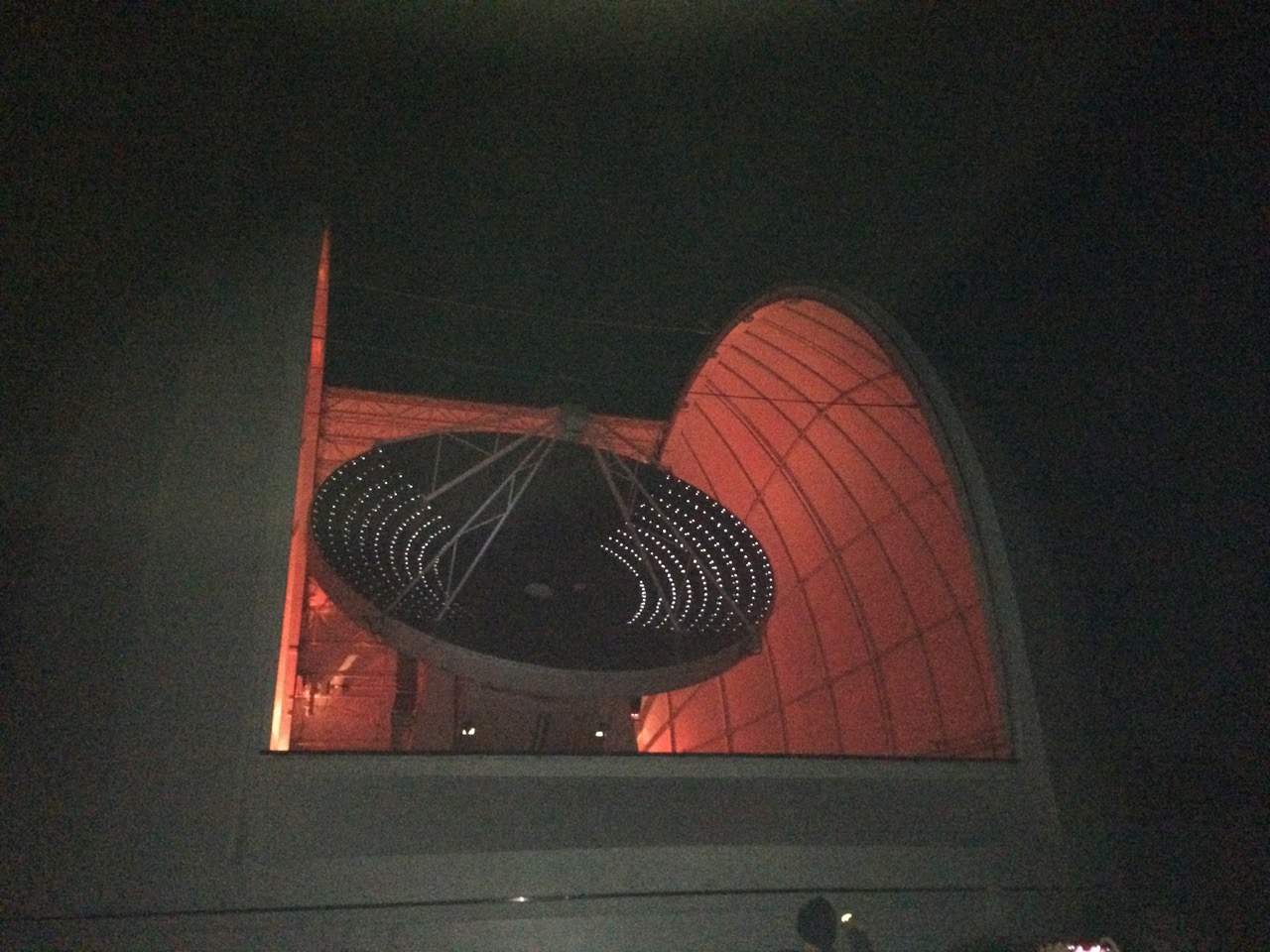 Radio telescope at night, with dome open and telescope back lit.