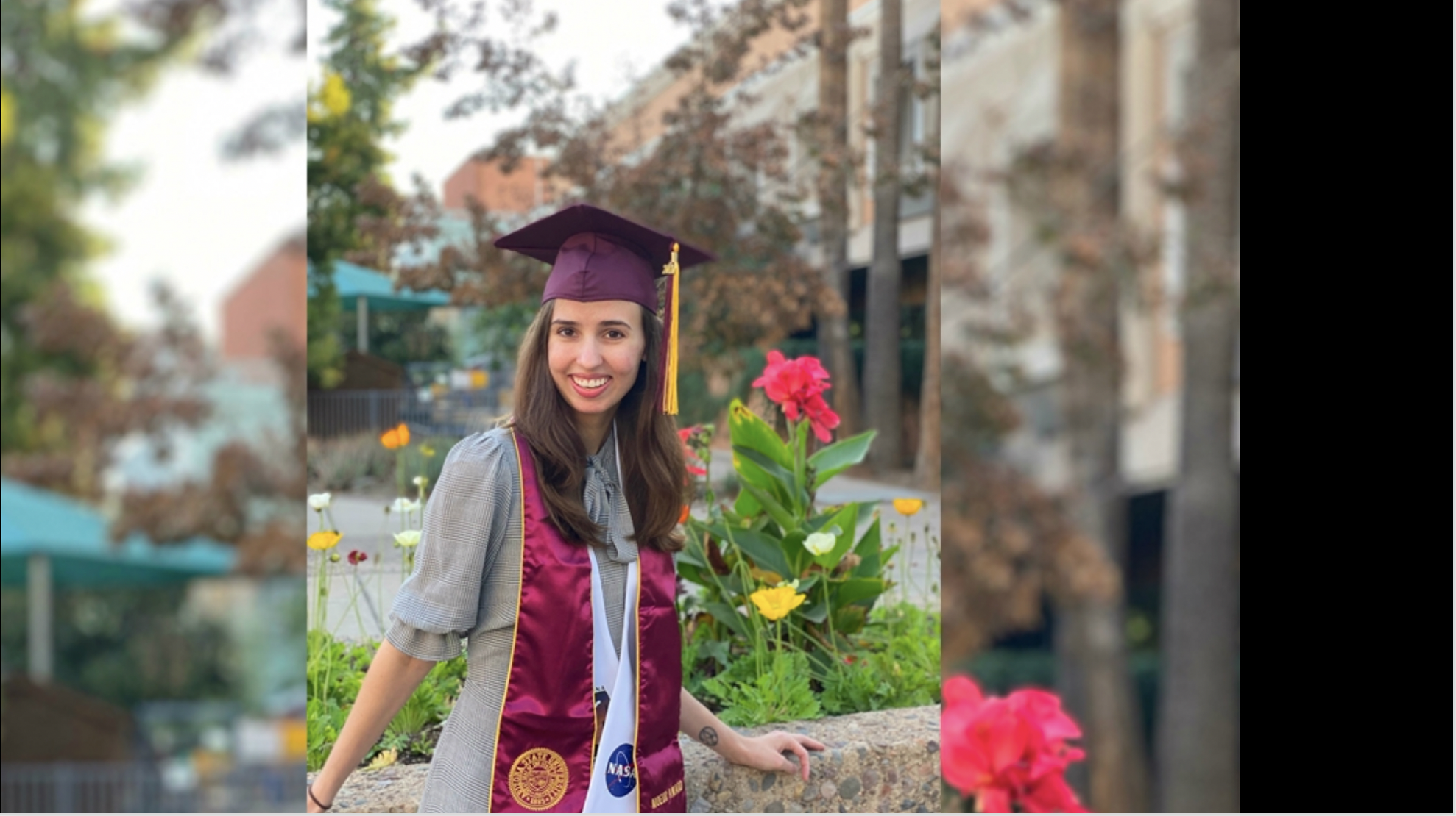 Elinor Saur in graduation cap and sash, posing outside by flowers.